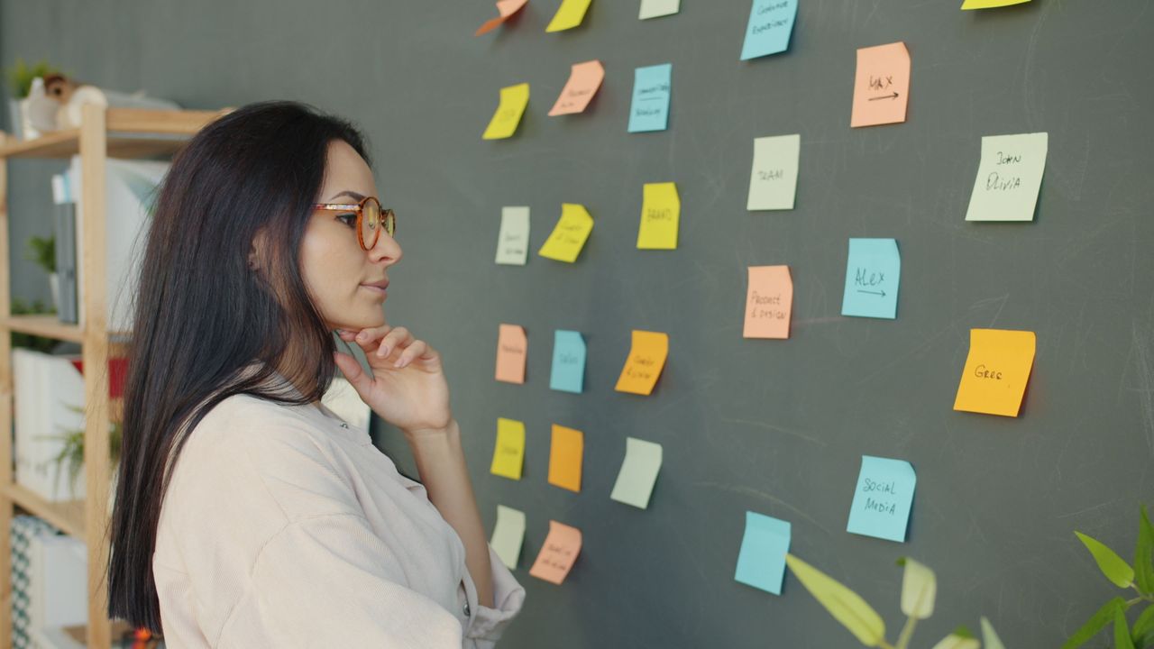 A woman analyzes colorful sticky notes on a chalkboard, planning and brainstorming ideas.